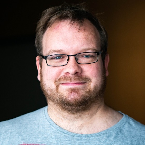 Christoph lächelt leicht in die Kamera. Er trägt kurze, dunkelblonde Haare, eine Brille und einen Drei-Tage-Bart.