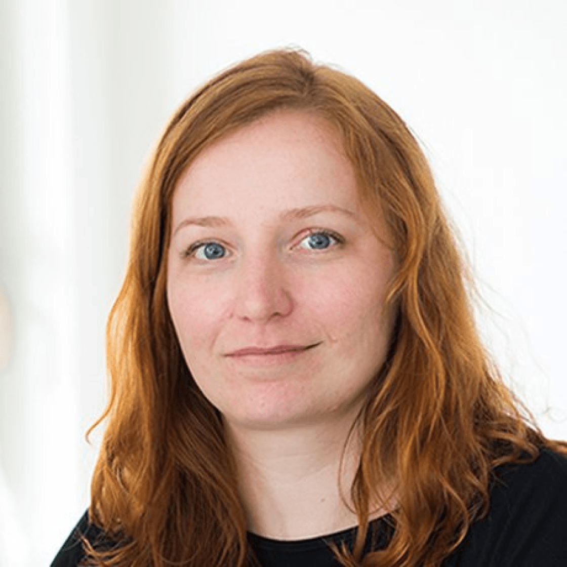 Anitas welligen roten Haare fallen ihr auf die Schulter und sie lächelt leicht.