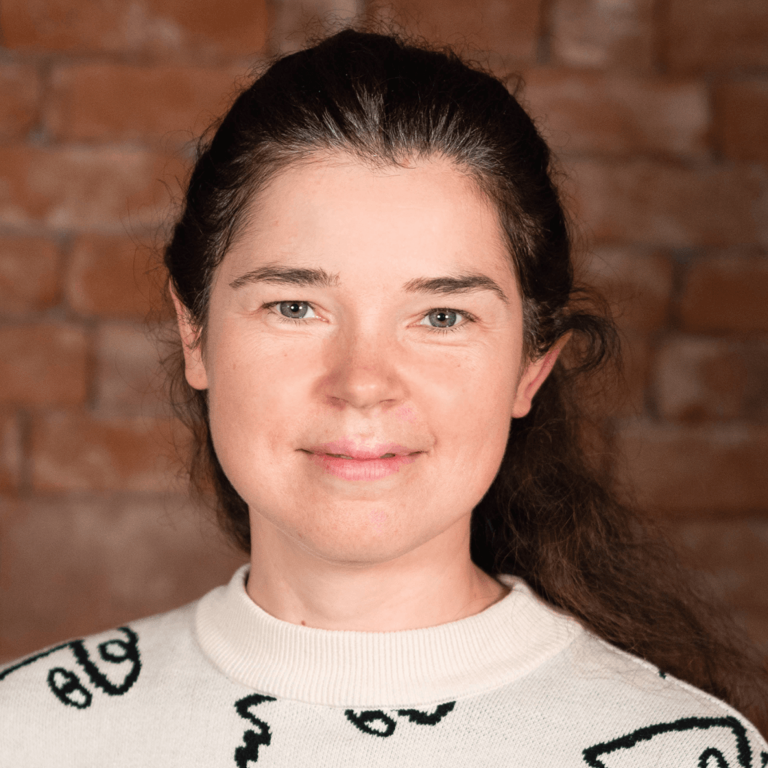 Carina trägt ihre langen dunklen Locken nach hinten gebunden und lächelt leicht.