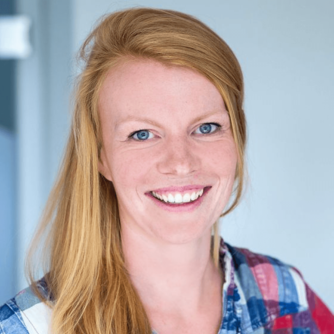 Carolin hat langes blondes Haar und lächelt breit.