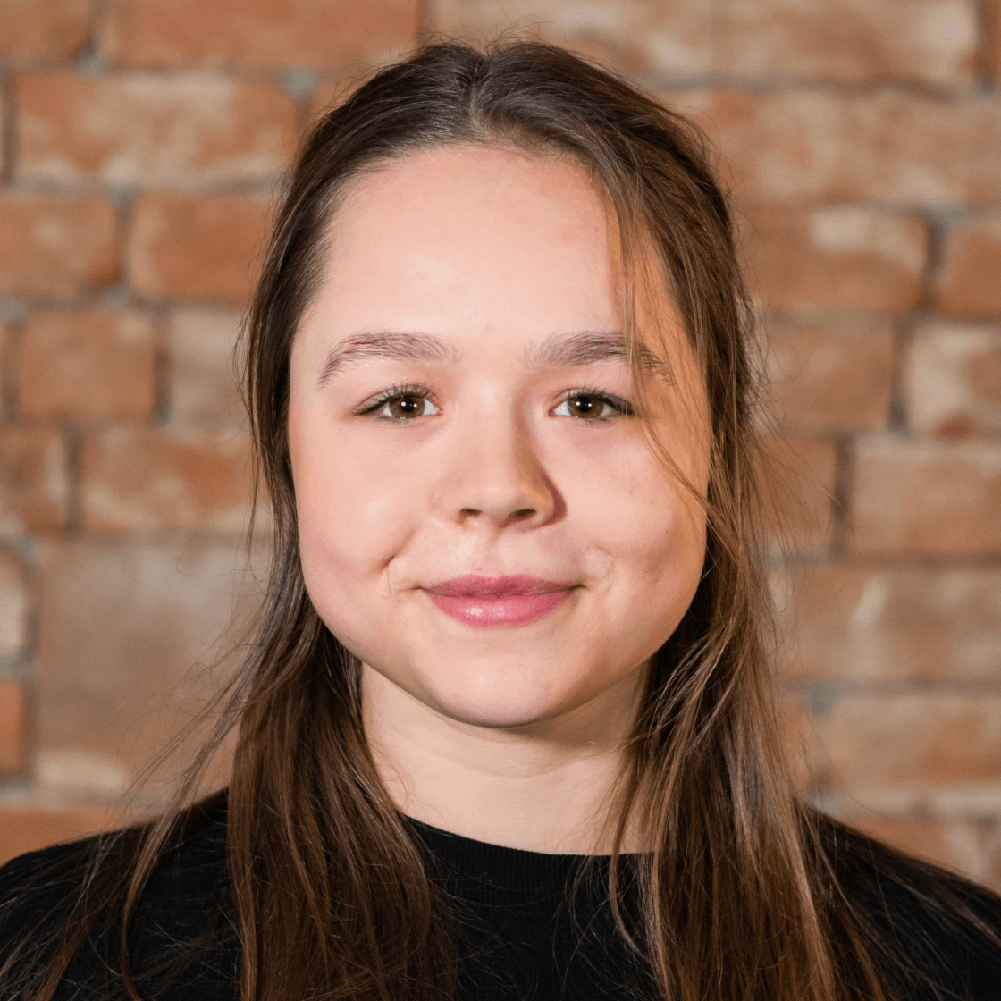 Lena hat langes braunes Haar und lächelt freundlich.