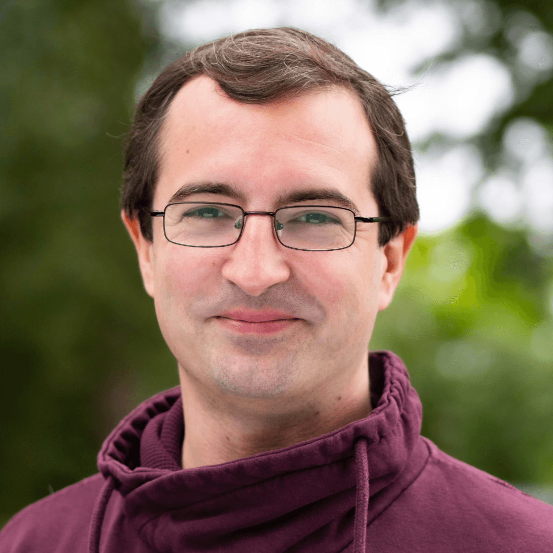 Marc hat braunes Haar und trägt eine Brille mit rechteckigen Gläsern und dunklem Gestell. 