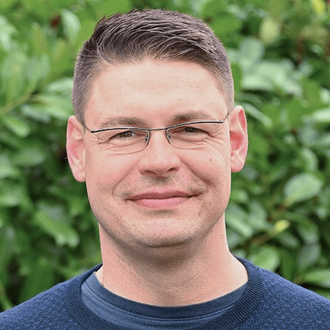 Marian hat kurzes nach oben gestyltes Haar und eine Brille. Er lächelt.
