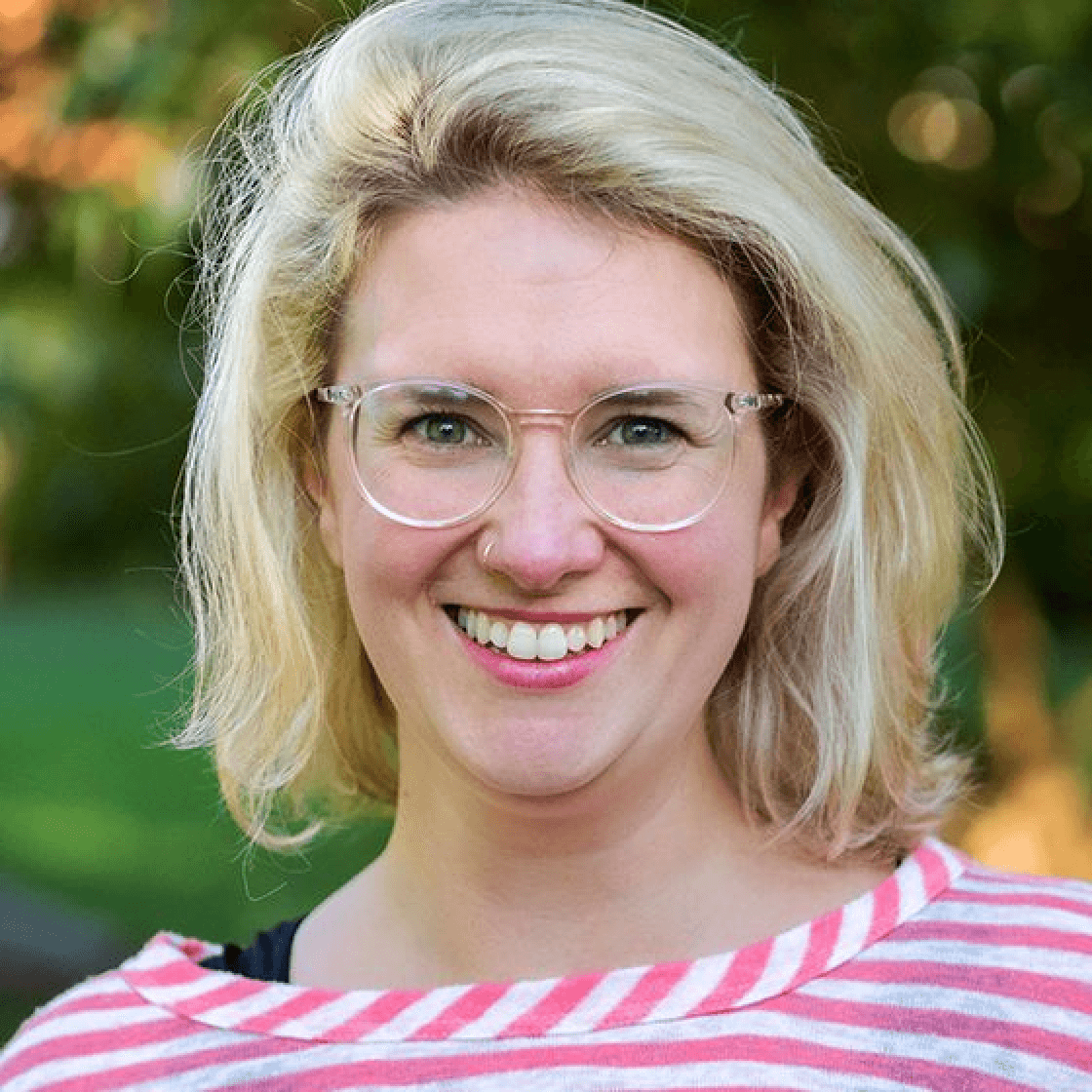 Marlen hat schulterlanges hellblondes Haar, eine Brille mit hellem Gestell und lächelt breit.