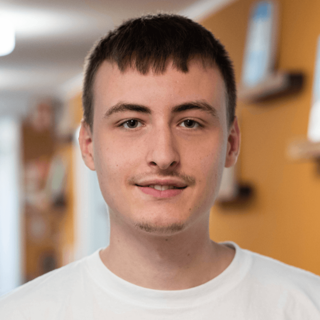 Philipp hat kurze dunkle Haare mit einem Pony. Er trägt einen Oberlippenbart und lächelt in die Kamera. 