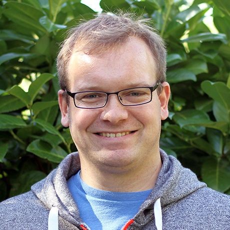 Christoph Bunge trägt kurze dunkelblonde Haare, eine dunkle Brille  und lächelt in die Kamera. 