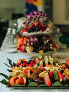Farbenfrohes Buffet mit frisch geschnittenem Obst wie Melonen, Trauben, Orangen und Beeren, dekoriert mit grünen Blättern und Blumen, bei einem Event.