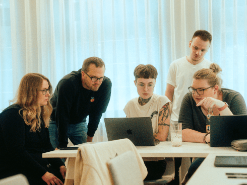 Team von MANDARIN bei einer kreativen Besprechung, konzentriert über Laptops arbeitend, in einem modernen Meetingraum mit Vorhängen und entspannter Atmosphäre.