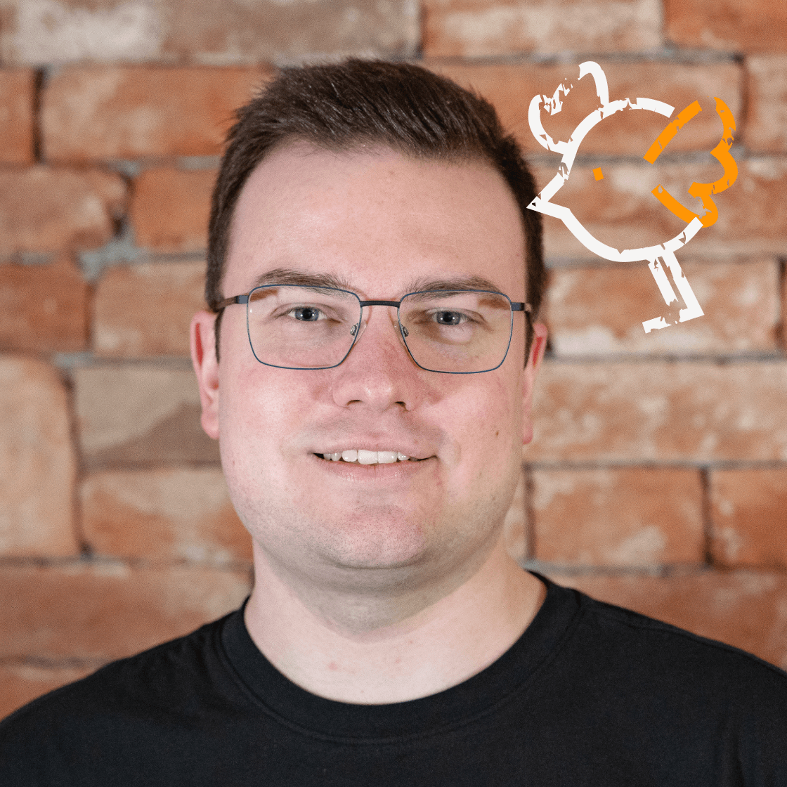 Dieses Porträt zeigt Hannes, einen Mann mit kurzem, dunkelblondem Haar, Brille und einem freundlichen Lächeln. Er trägt ein schwarzes Oberteil, das für einen modernen und professionellen Look sorgt. Der warme Backstein-Hintergrund schafft eine authentische, stilvolle Atmosphäre. Ein besonderes Detail: die gezeichnete Vogel-Illustration in der oberen rechten Ecke, die dem Bild eine kreative und verspielte Note verleiht.