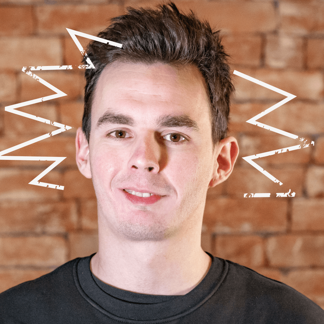 Dieses Porträt zeigt Tom, einen jungen Mann mit dunklem, vollem Haar und einem selbstbewussten Ausdruck. Er trägt ein schwarzes Oberteil, das für einen modernen und zeitlosen Look sorgt. Der warme Backstein-Hintergrund schafft eine authentische, urbane Atmosphäre. Ein besonderes Highlight: Die gezeichneten dynamischen Linien um seinen Kopf verleihen dem Bild eine kreative und energiegeladene Note.