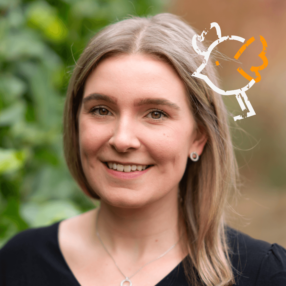  „Porträt von Charleen mit schulterlangem, blondem Haar und schwarzem Oberteil. Sie trägt eine dezente Halskette und Ohrstecker. Rechts oben im Bild ist ein stilisierter, weiß-orangefarbener Vogel zu sehen – ein grafisches Element, das für Kommunikation, Leichtigkeit oder Kreativität steht. Der Hintergrund zeigt eine grüne, natürliche Umgebung mit weichem Fokus.