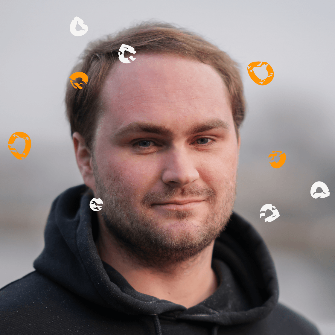 Porträt von Max mit kurzem, hellbraunem Haar und dunklem Hoodie. Er blickt ruhig und selbstbewusst in die Kamera. Um ihn herum schweben stilisierte, orangene und weiße Kreiselemente – grafische Symbole, die Bewegung, Kreativität oder Ideenfluss visualisieren. Der Hintergrund ist weichgezeichnet und zeigt eine ruhige Außenkulisse in Grautönen