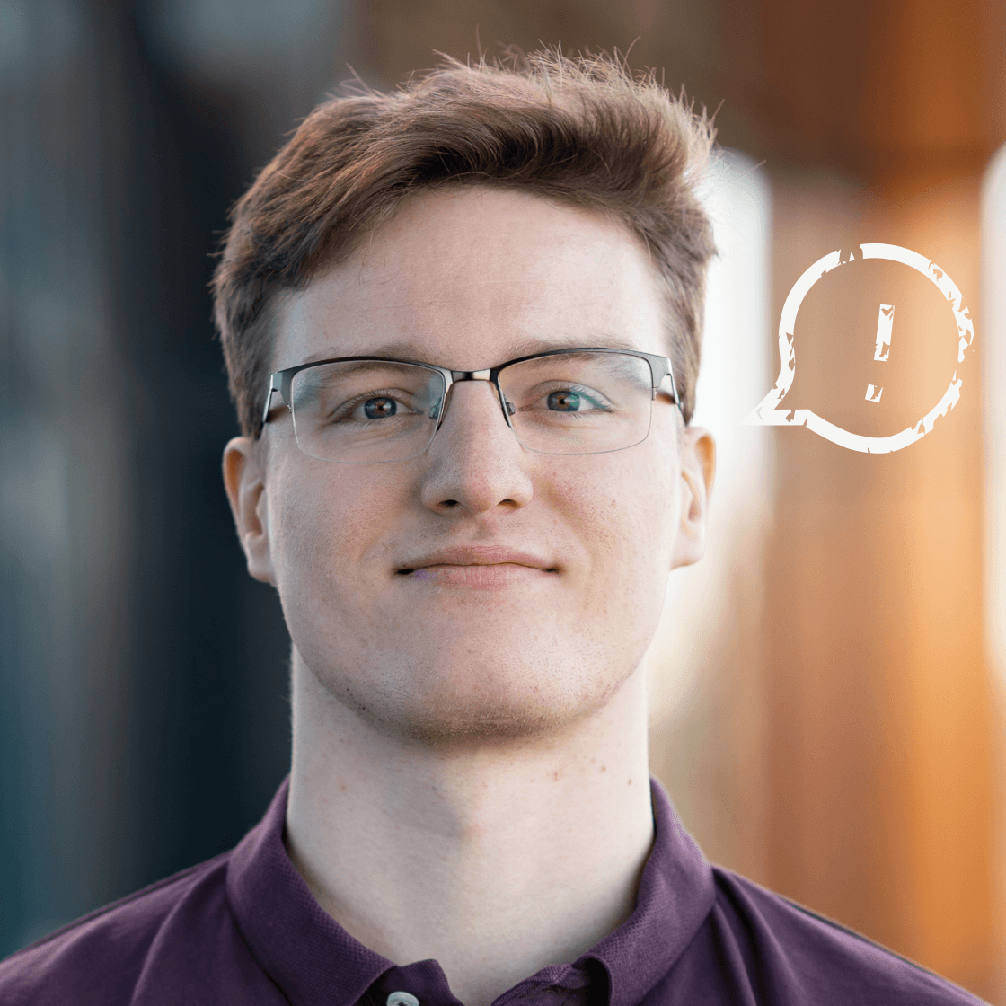Porträt von Erik mit kurzem, braunem Haar, Brille und weinrotem Poloshirt. Er blickt ruhig und fokussiert in die Kamera. Rechts neben ihm ist eine stilisierte, weiße Sprechblase mit Ausrufezeichen zu sehen – ein Symbol für Kommunikation, Information oder wichtige Impulse. Der Hintergrund zeigt eine moderne, unscharfe Outdoor-Architektur.