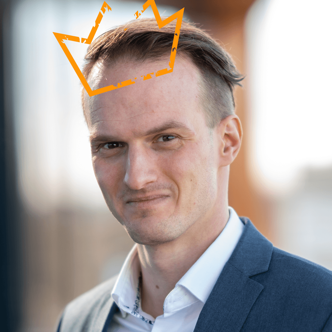 Porträt von Gerard mit kurzem, nach hinten frisiertem Haar und blauem Anzug. Über seinem Kopf schwebt eine stilisierte, orangefarbene Krone – Symbol für Führungsstärke, Verantwortung oder besondere Auszeichnung. Gerard blickt souverän in die Kamera. Der Hintergrund ist unscharf und zeigt eine lichtdurchflutete Outdoor-Szenerie.