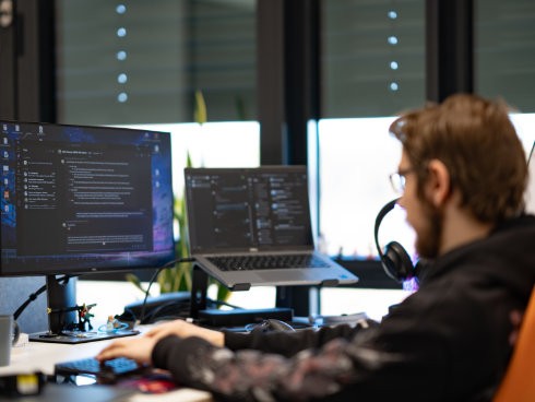 IT-Experte programmiert im Dark Mode mit zwei Monitoren und Headset im Büro.