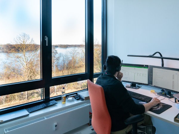 IT-Mitarbeiter arbeitet am Schreibtisch mit Monitoren und Blick auf den See.