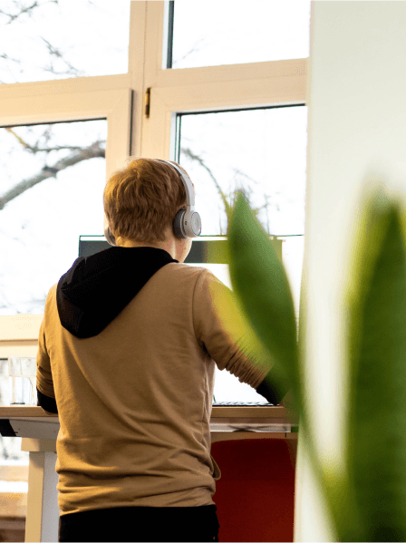 Ember arbeitet konzentriert mit Kopfhörern am Stehschreibtisch im Büro.