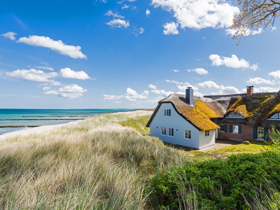 Ein Haus umgeben von Strandhafer, links das Meer.