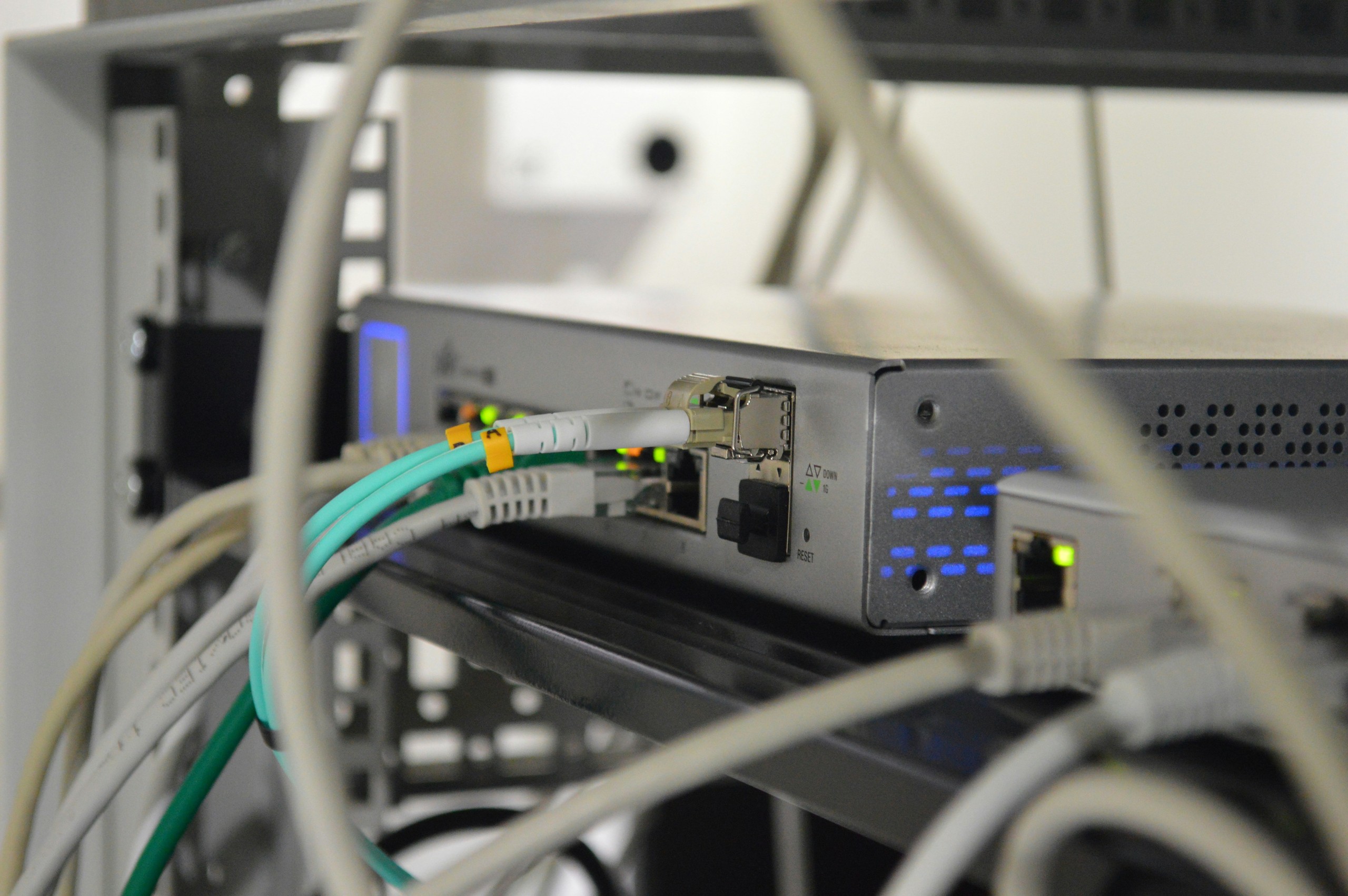 Nahaufnahme von Netzwerkgeräten und Verkabelung in einem Serverraum, die LED-Lichter und verschiedene Netzwerkanschlüsse zeigen.