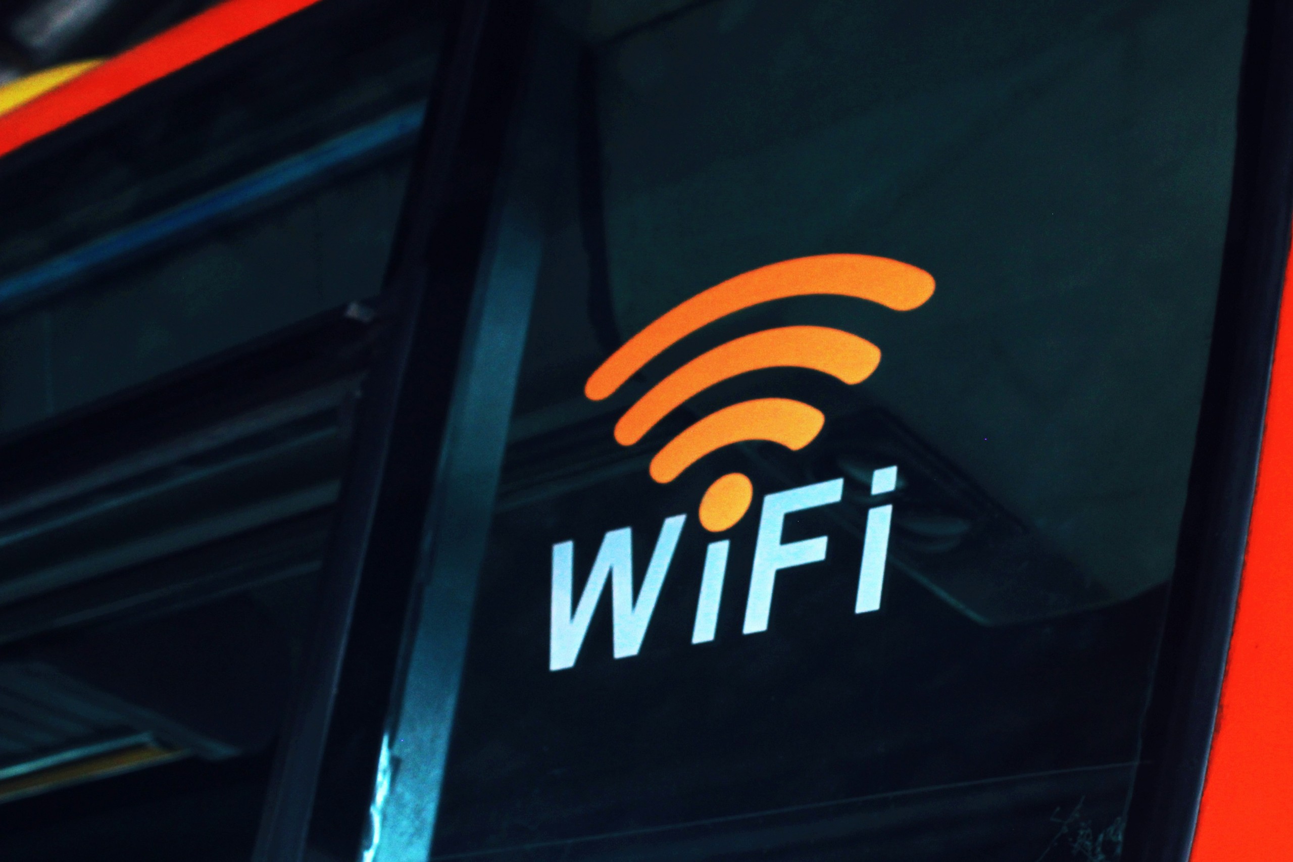 WiFi-Symbol in Orange und Weiß auf einer Glasoberfläche, möglicherweise ein Hinweis auf verfügbares drahtloses Internet in einem öffentlichen Verkehrsmittel.