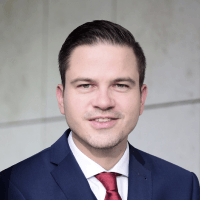Porträt eines Mannes in einem dunklen Anzug mit roter Krawatte vor einem neutralen Hintergrund. Professionelle Darstellung für geschäftliche oder offizielle Zwecke.