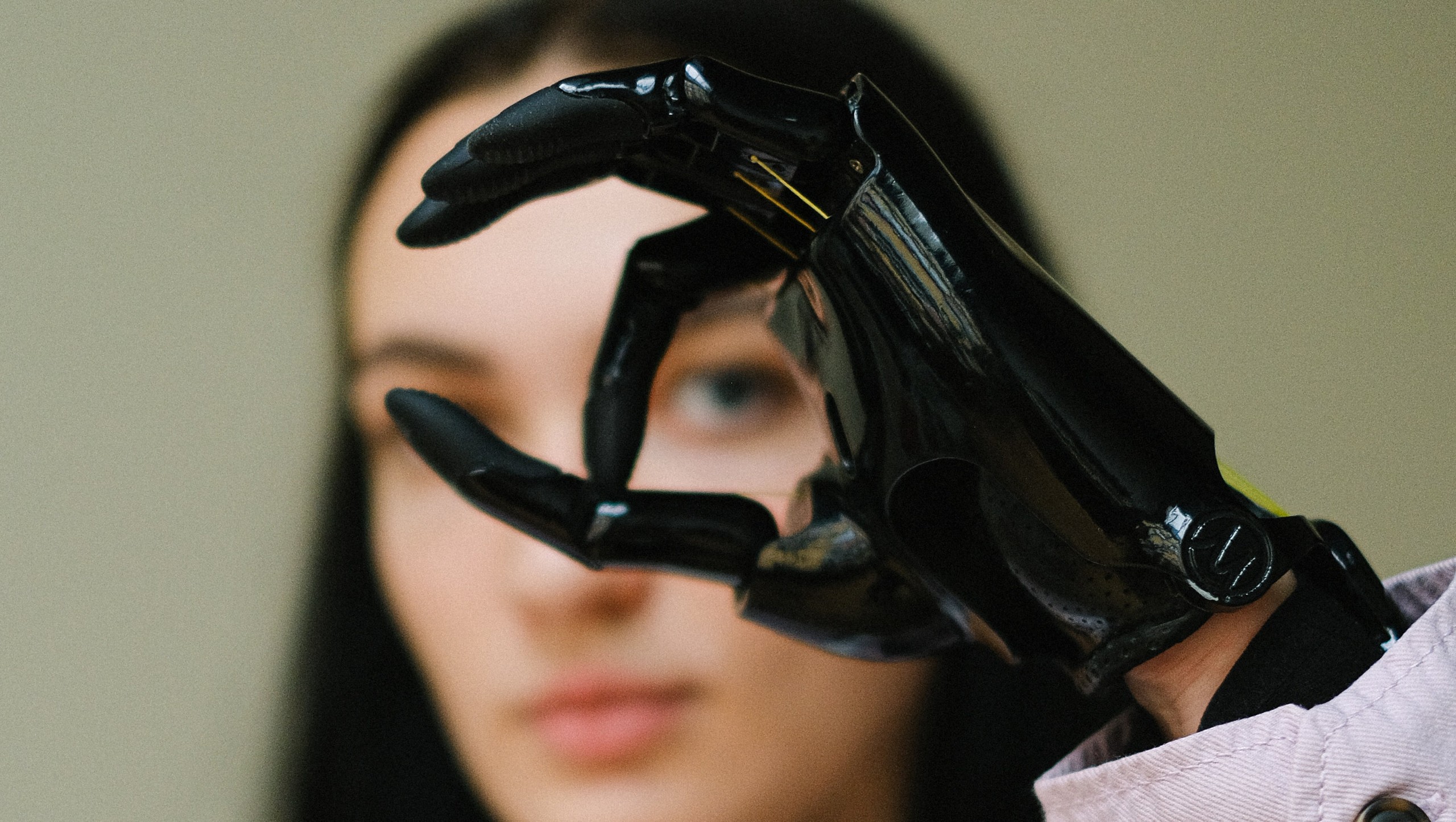 Fokus auf eine schwarze High-Tech-Prothese in einer Handhaltung, mit einer unscharfen Frau im Hintergrund, die die moderne Technologie und Barrierefreiheit symbolisiert.
