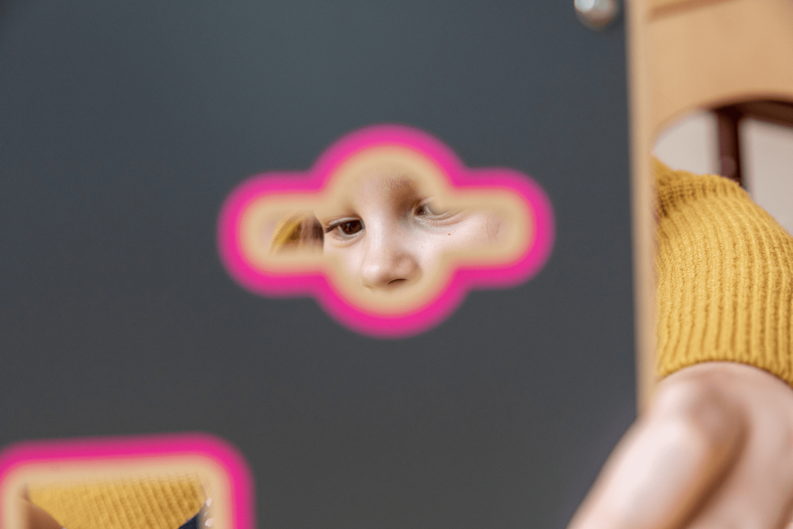 Kind blickt konzentriert durch Spieltafel mit Formenausschnitt – gezielte Förderung von Wahrnehmung und Kreativität in der frühkindlichen Bildung beim Internationalen Bund.