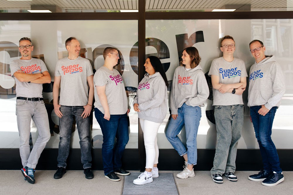Sieben Menschen mit Super Social-T-Shirts vor einer Milchglaswand