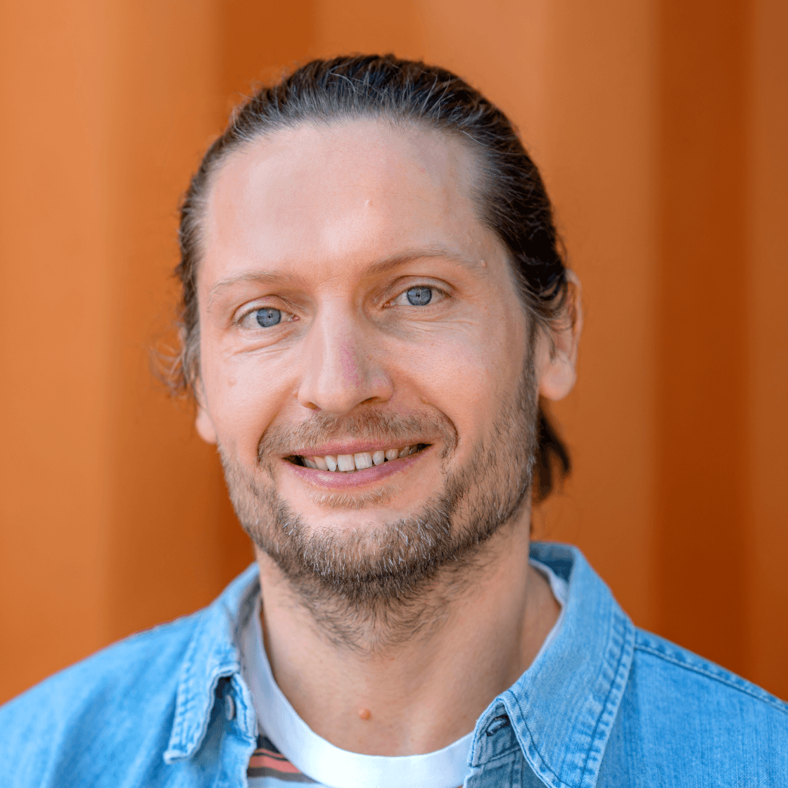 Portrait von Karsten, Accountmanager bei MANDARIN, lächelnd vor orangefarbenem Hintergrund