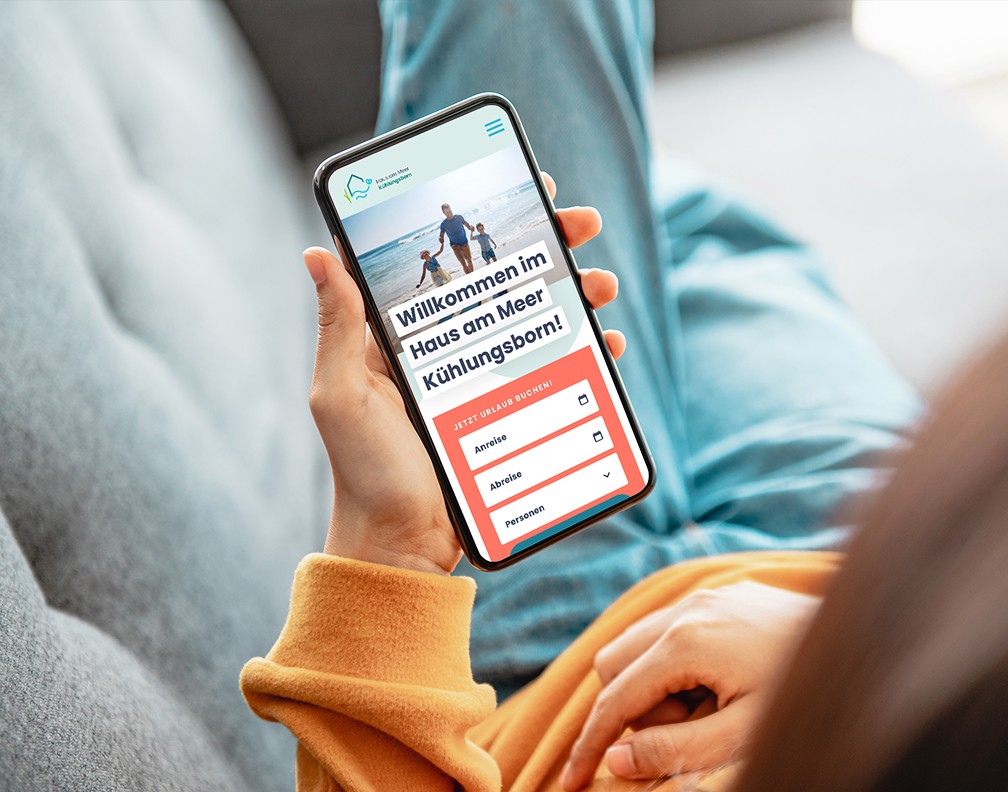 Person mit Handy in der Hand, auf dem Handy ist die Website des Hauses am Meer geöffnet