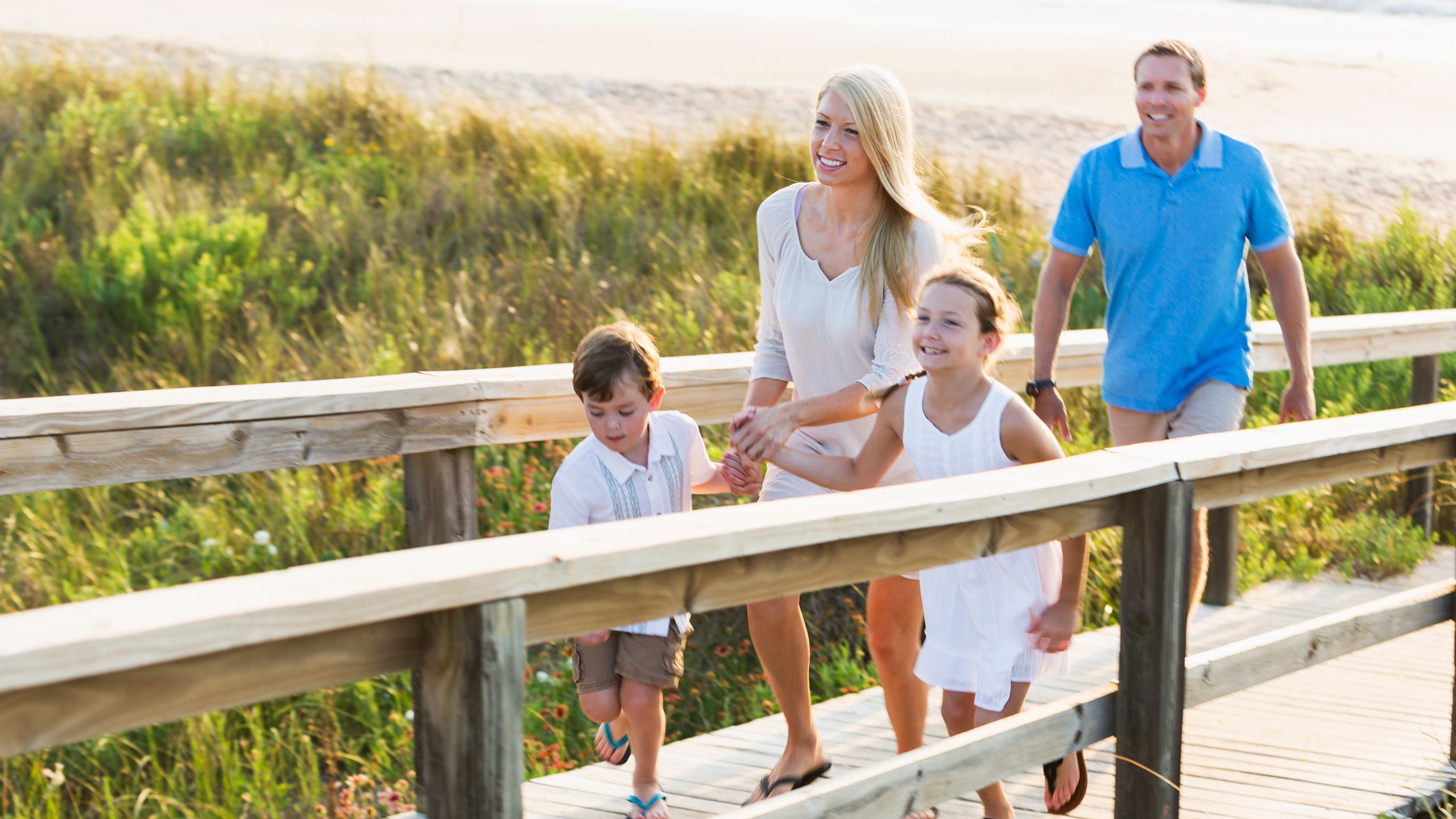 Zwei Erwachsene und zwei Kinder laufen einen Steg hinauf, im Hintergrund Strand und Meer