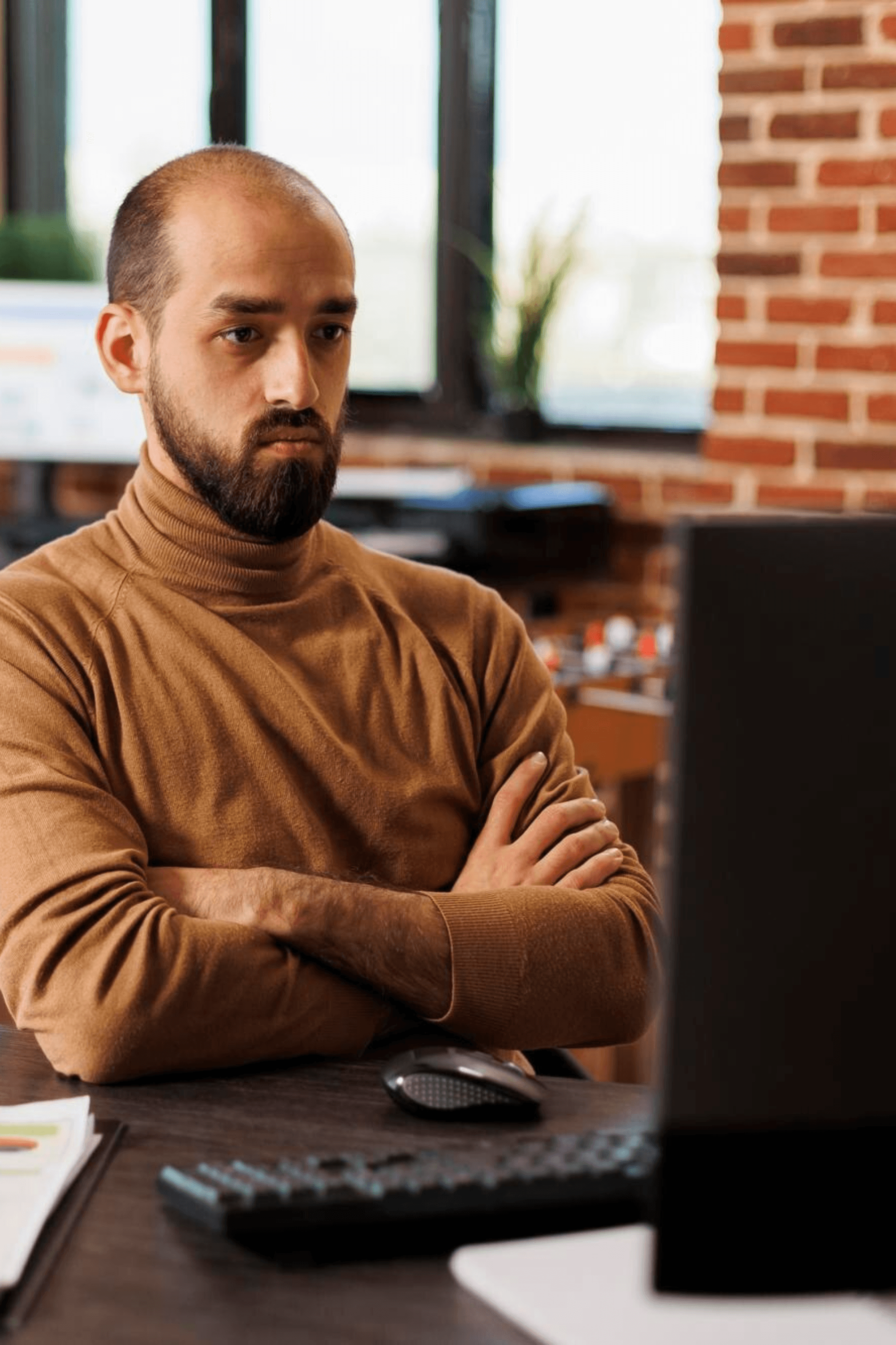 Junger Geschäftsmann sitzt mit verschränkten Armen im Büro und schaut auf den Computermonitor, während er Finanzstatistiken überprüft. Mitarbeiter des Marketingbüros Brainstorming-Management-Ideen.